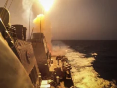 Tanie drony, deficytowe pociski: czego trzeba, by obrona powietrzna wytrzymała A missile leaves a warship's deck in a bright burst of flame and smoke, lighting up the ship's superstructure and wake at dusk