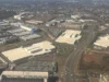 Who pays for the grid that data centres need? Aerial view of large flat-roofed data centre buildings spread among roads and commercial sites under a partly cloudy sky.