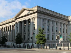 Pourquoi les États riches paient plus cher pour emprunter, et qui en fait les frais Wide view of the long colonnaded granite facade of the US Treasury Building under a blue sky, with trees and a street in front