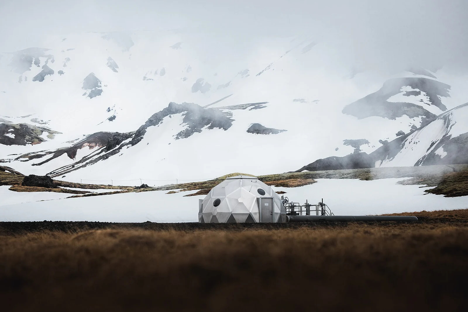 Una pequeña cúpula geodésica que alberga un pozo de inyección de CO2 en una llanura bajo montañas nevadas en Islandia