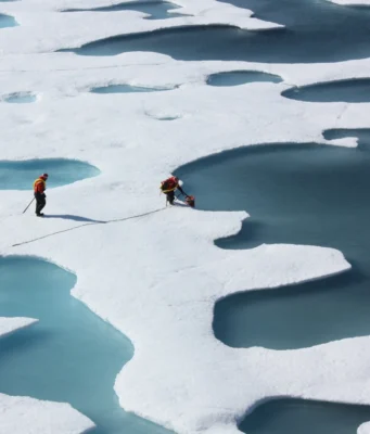 Can the world cool back down after 1.5°C? Turquoise meltwater ponds spread across white Arctic sea ice, with two researchers standing on the ice