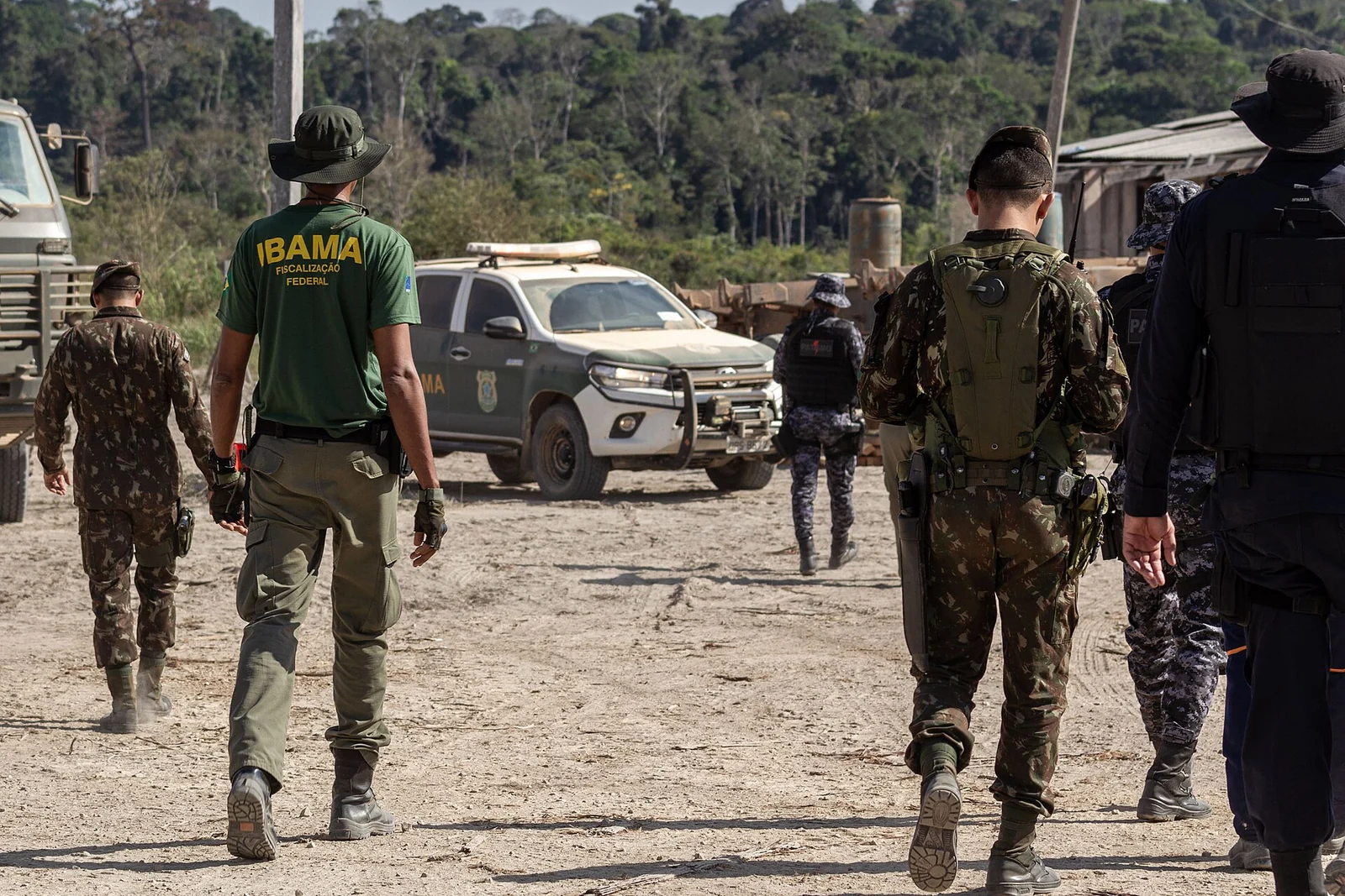 Un agente del Ibama camina con soldados uniformados junto a vehículos de fiscalización en un claro al borde del bosque