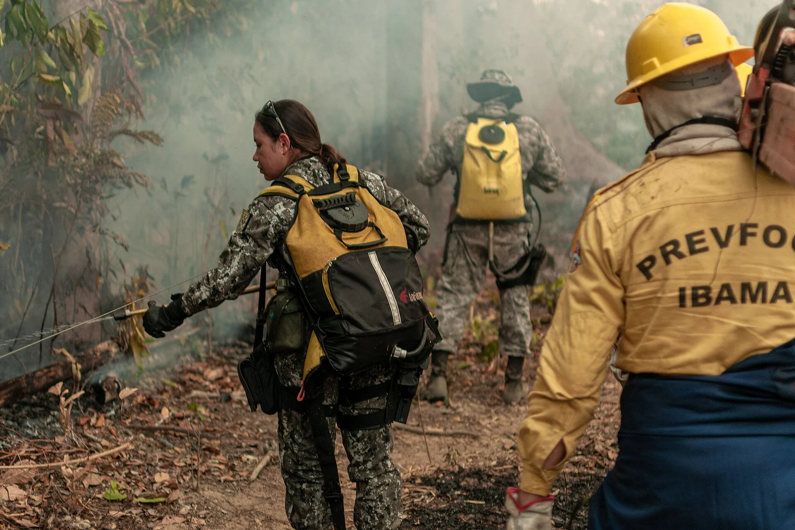 Bomberos con uniformes del Prevfogo Ibama y soldados con mochilas trabajan entre el humo en el sotobosque quemado
