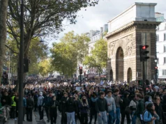 Cómo las protestas escolares de Francia confluyeron con la revuelta por el coste de la vida A large crowd of marchers filling a tree-lined Paris boulevard beside the stone triumphal arch of the Porte Saint-Martin