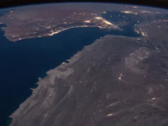 How the world absorbed the Hormuz oil shock Night view from orbit of the Gulf of Oman and the Strait of Hormuz, with city lights along the coasts and the curve of the Earth on the horizon