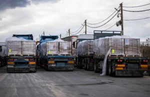 The arithmetic of a ration cut A line of flatbed trucks loaded with aid pallets parked at a desert crossing point.