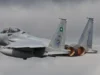 Ce que les dépenses militaires de l’Arabie saoudite ne peuvent garantir A grey Royal Saudi Air Force F-15SA fighter jet flying with both afterburners glowing against a dark cloudy sky.