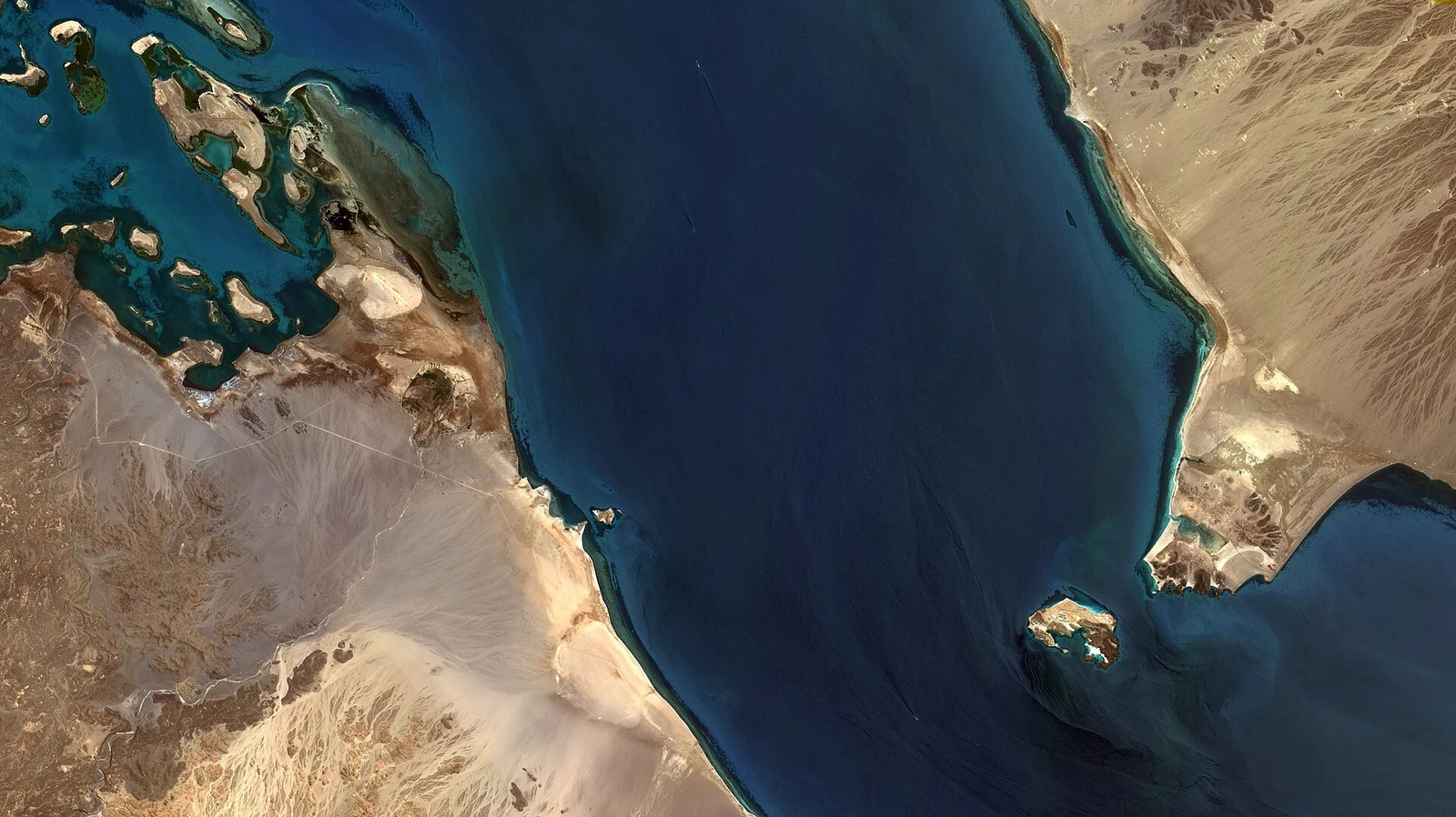 Vue satellite d'un étroit détroit bleu entre des côtes désertiques, avec une petite île près de la rive droite.