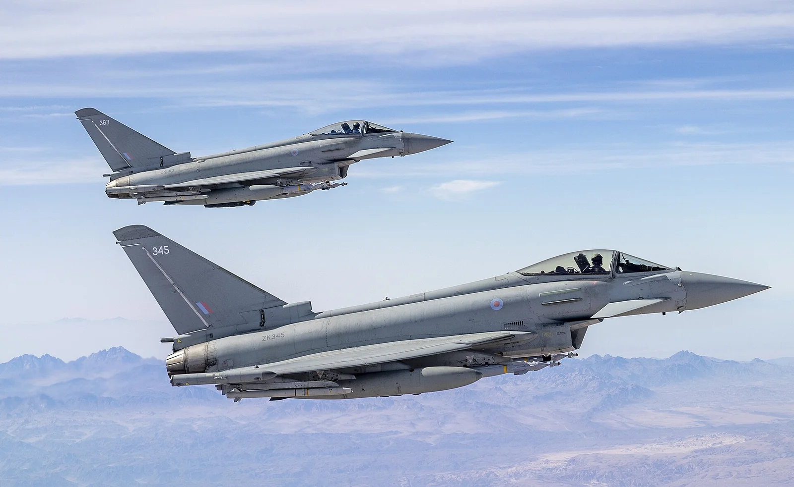 Deux chasseurs Eurofighter Typhoon gris de la RAF volant en formation au-dessus d'une chaîne de montagnes voilée de brume.