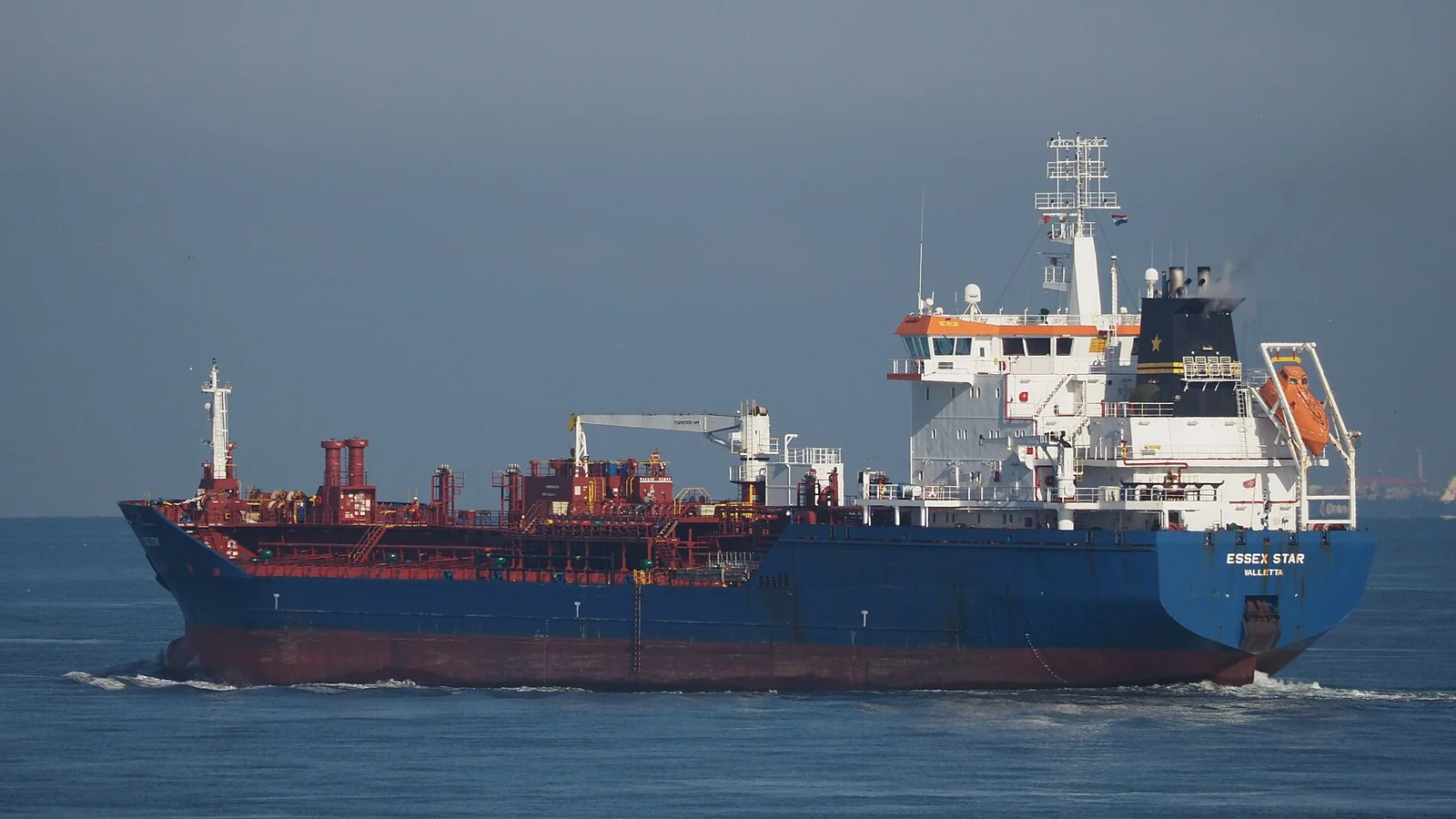 Un petrolero de casco azul con superestructura blanca navega por aguas de un verde grisáceo